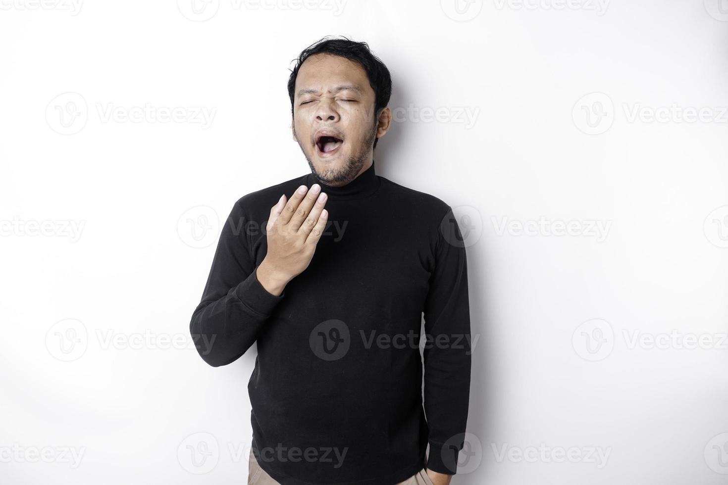 retrato de soñoliento atractivo asiático hombre vistiendo un negro camisa, sensación cansado después noche sin dormir, bostezando, cubierta abrió boca con palma foto