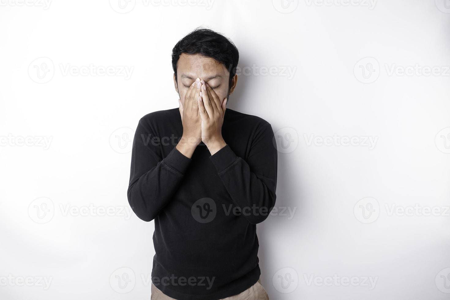 retrato de soñoliento atractivo asiático hombre vistiendo un negro camisa, sensación cansado después noche sin dormir, bostezando, cubierta abrió boca con palma foto