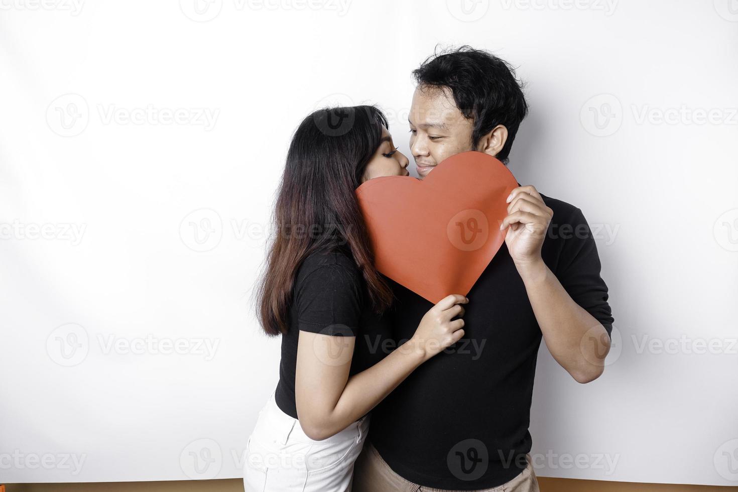 un Pareja en amor sostiene un papel rojo corazón, cubierta su caras. contento San Valentín día foto