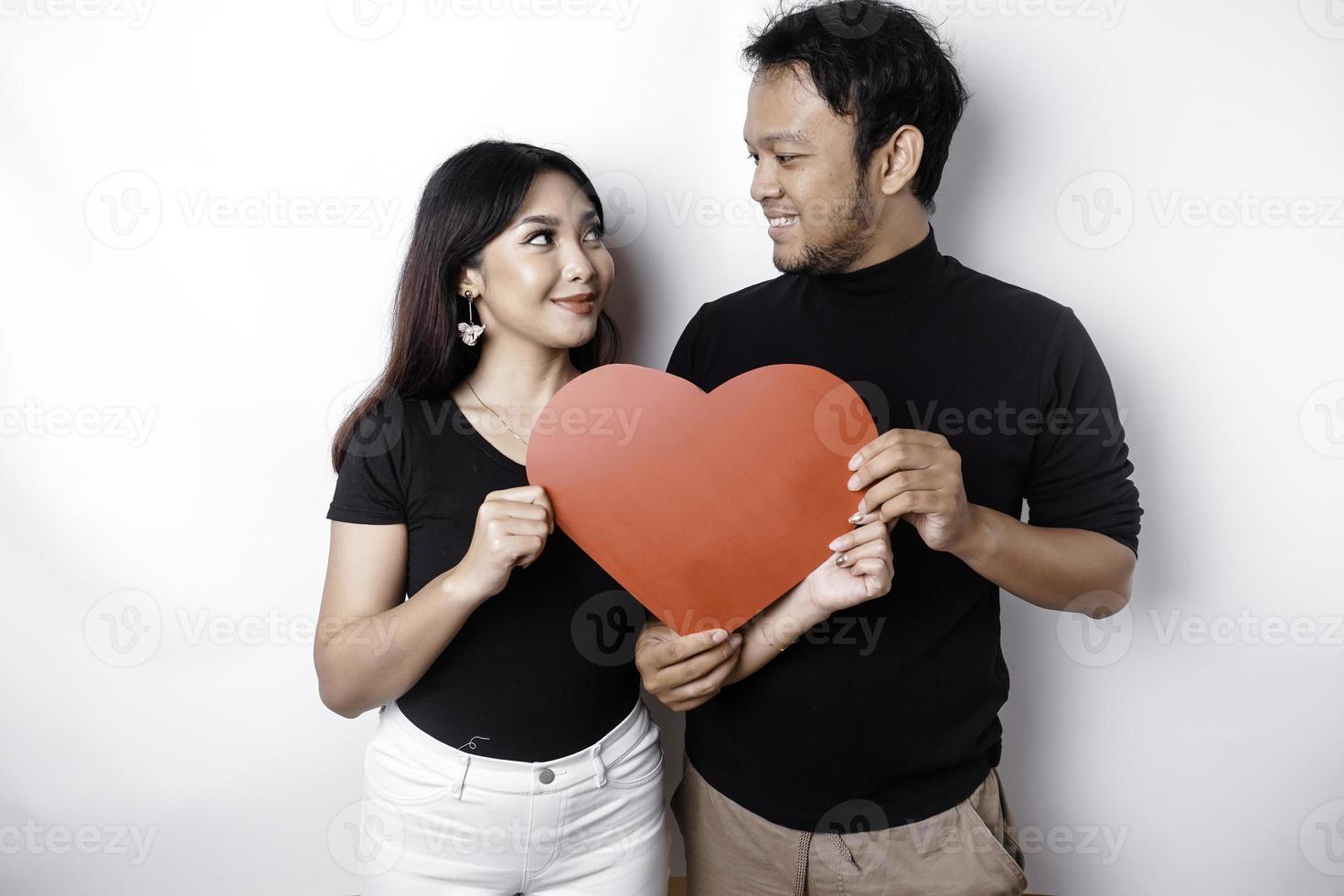 A young Asian couple smiling and holding red heart-shaped paper, isolated by white background photo