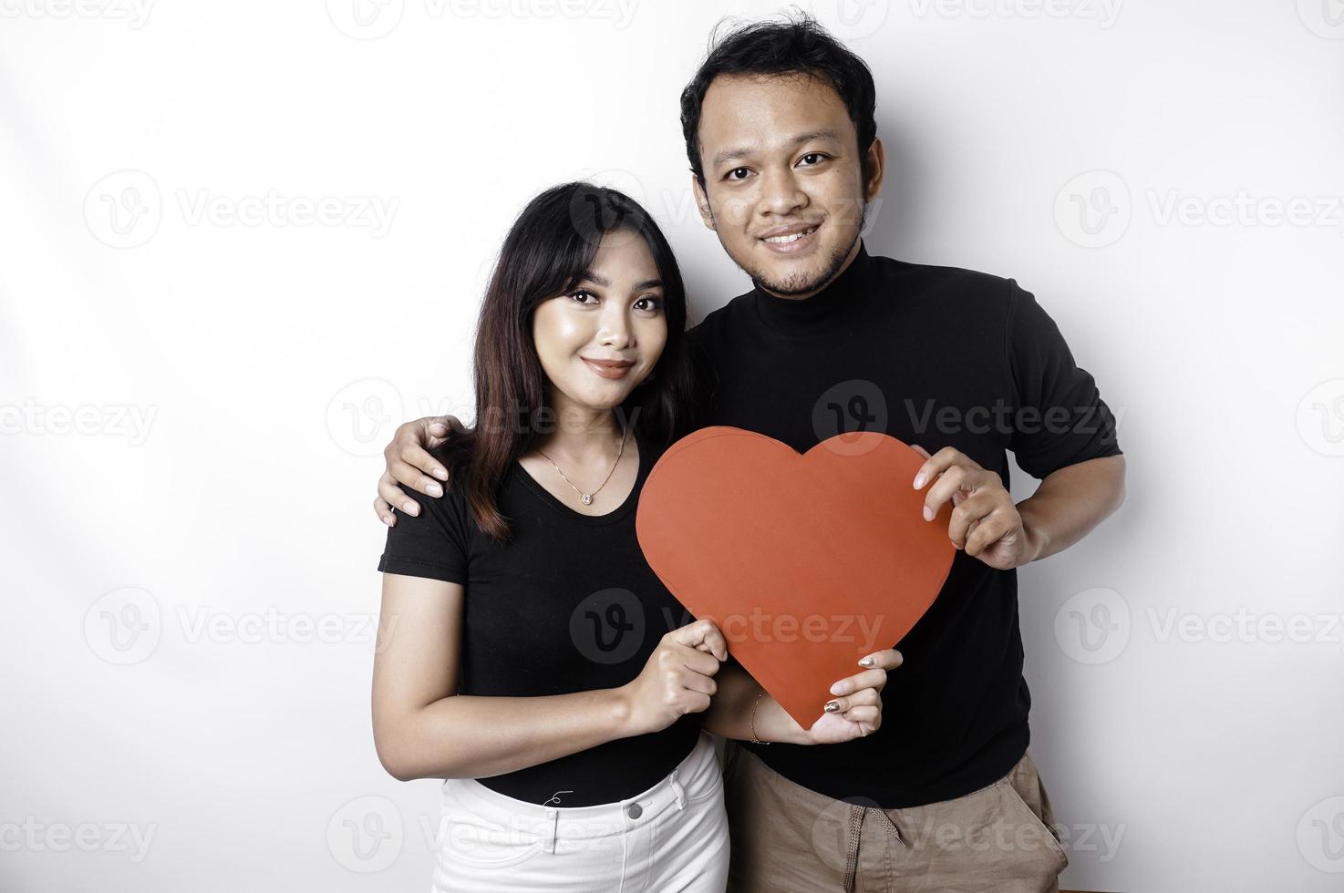 A young Asian couple smiling and holding red heart-shaped paper, isolated by white background photo