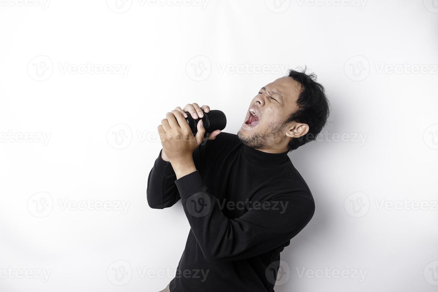 Portrait of carefree Asian man, having fun karaoke, singing in microphone while standing over white background photo