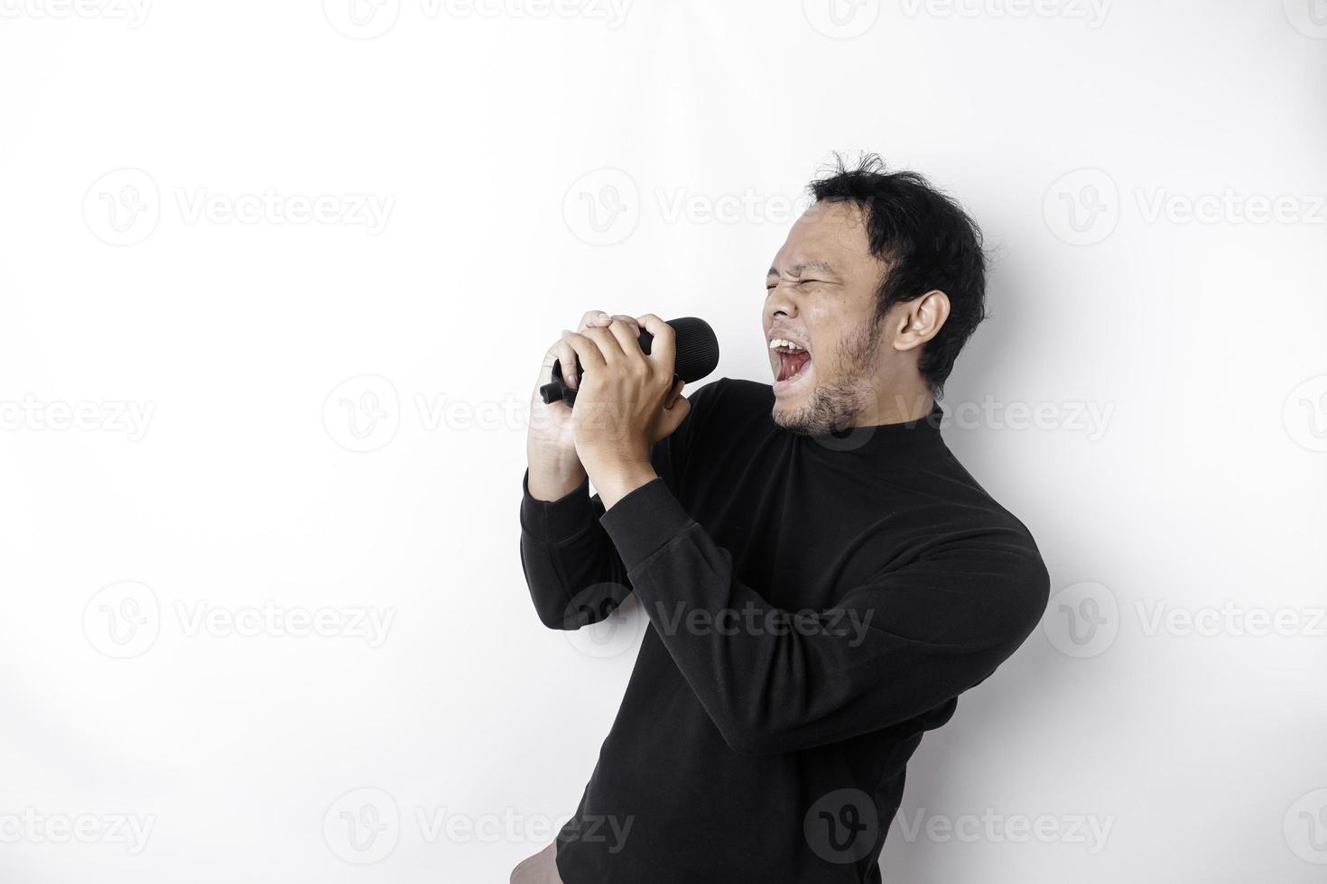 Portrait of carefree Asian man, having fun karaoke, singing in microphone while standing over white background photo