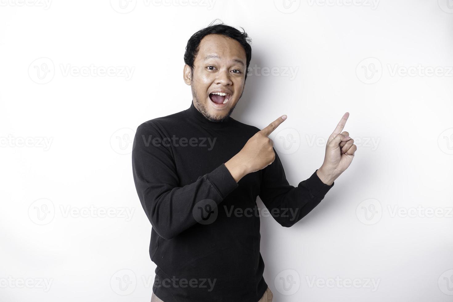 Excited Asian man wearing black shirt pointing at the copy space beside him, isolated by white background photo