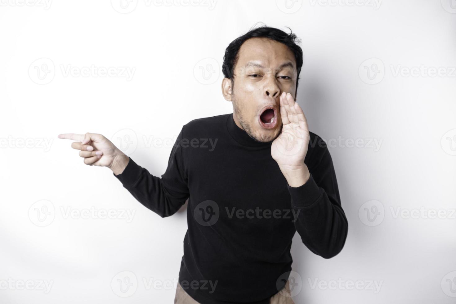 Shocked Asian man wearing black shirt pointing at the copy space beside him, isolated by white background photo