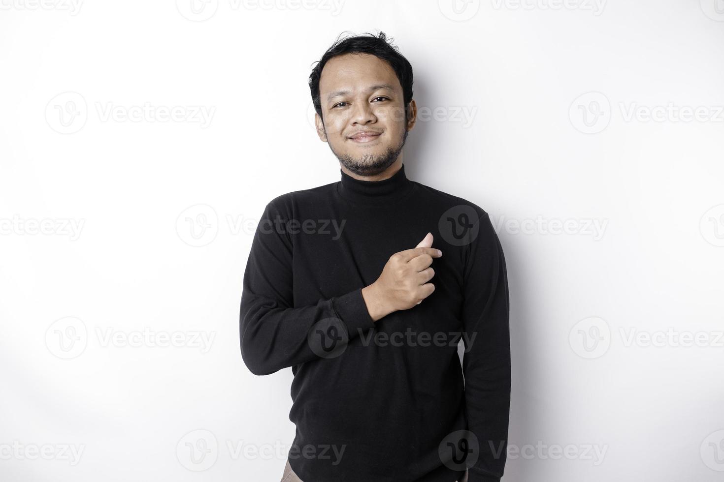 A happy young Asian man wearing a black shirt feels romantic shapes heart gesture expressing tender feelings photo