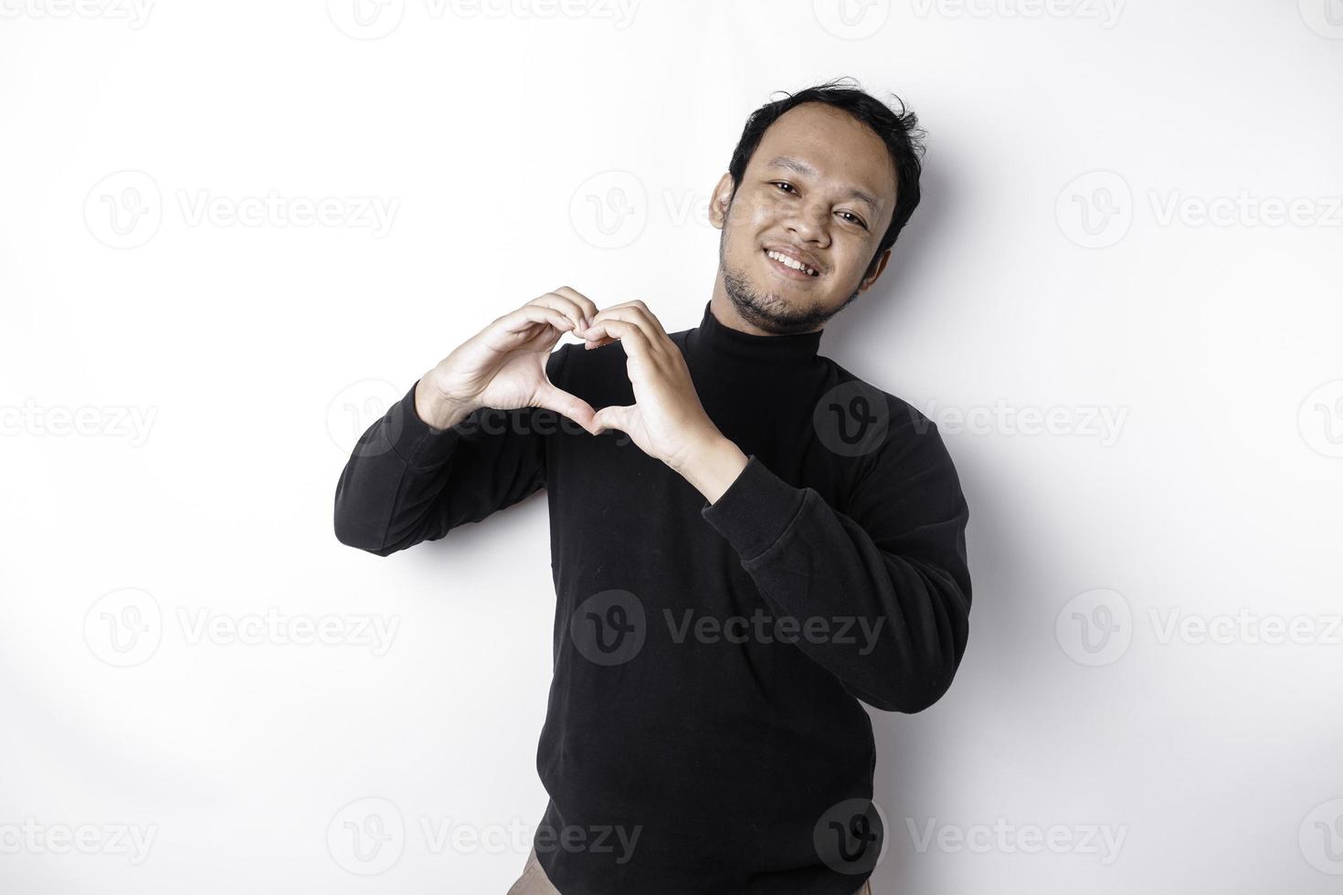 un contento joven asiático hombre vistiendo un negro camisa siente romántico formas corazón gesto expresando oferta sentimientos foto