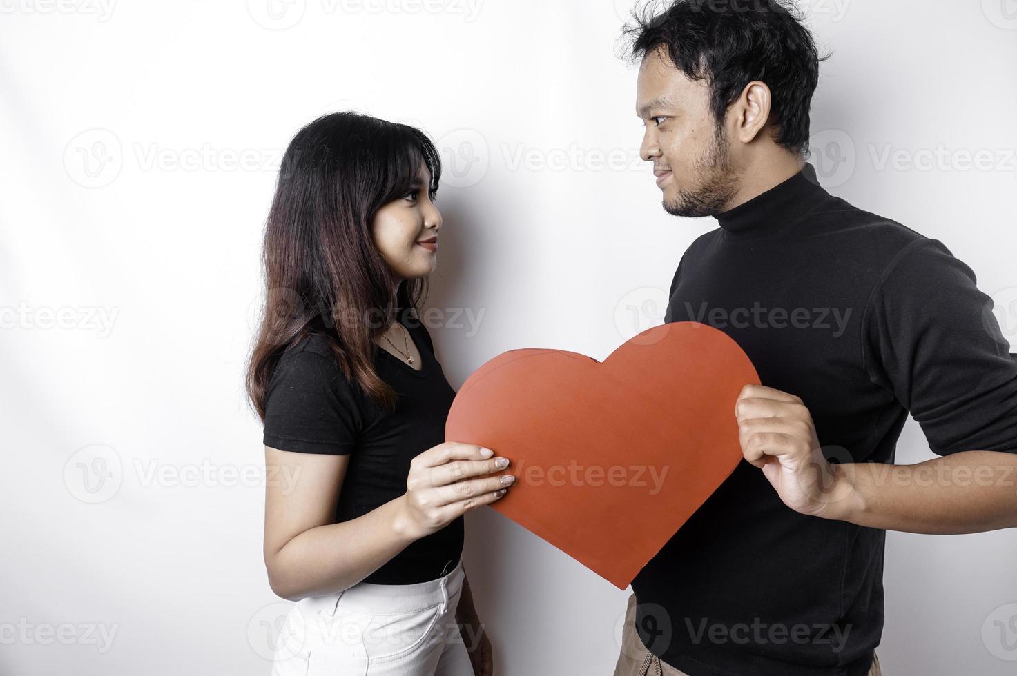 A young Asian couple smiling and holding red heart-shaped paper, isolated by white background photo