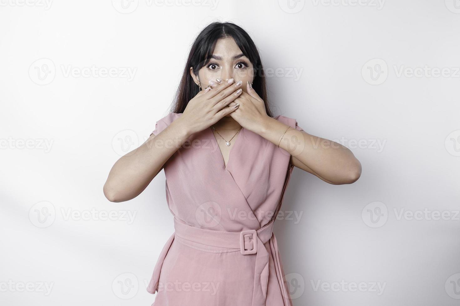 Surprised young Asian woman covering mouth with hands and staring at camera while standing against white background photo