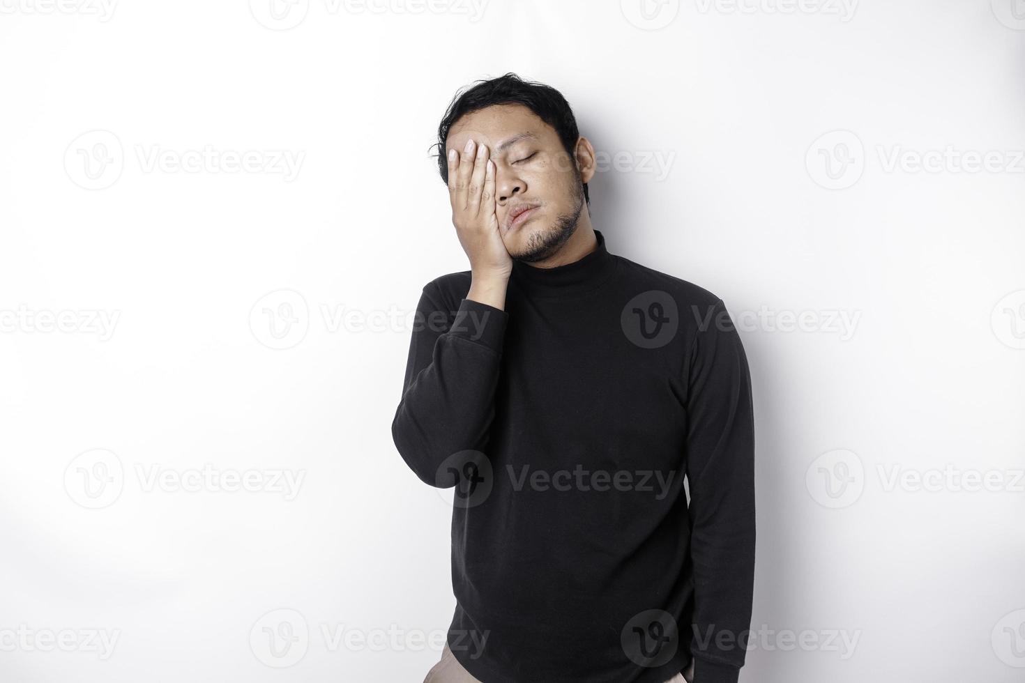 Portrait of sleepy attractive Asian man wearing a black shirt, feeling tired after night without sleep, yawning, covering opened mouth with palm photo