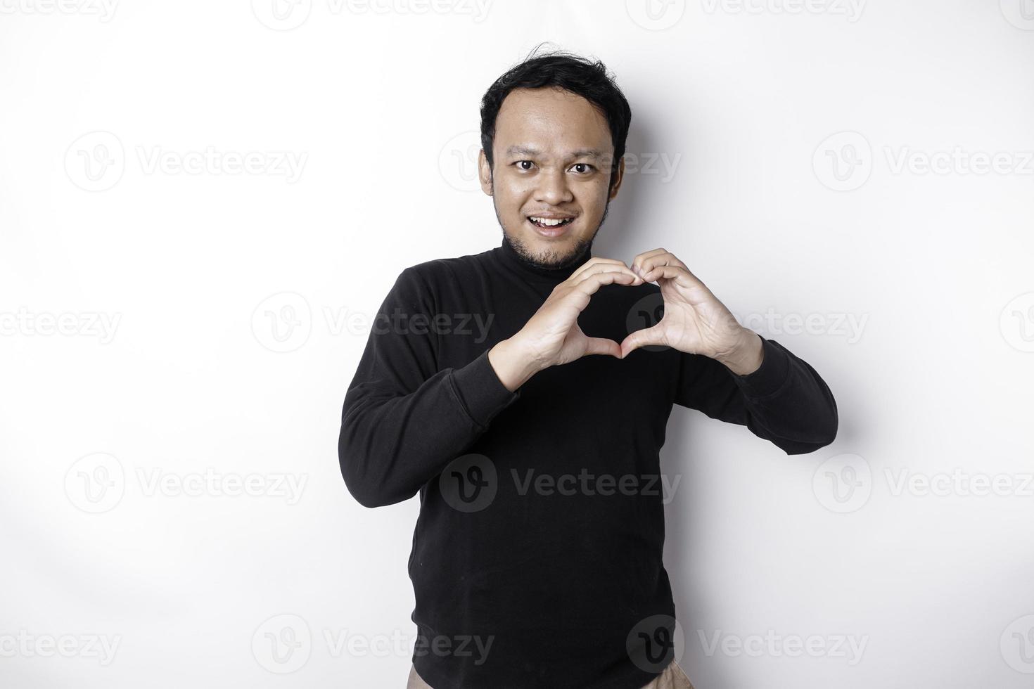 A happy young Asian man wearing a black shirt feels romantic shapes heart gesture expressing tender feelings photo