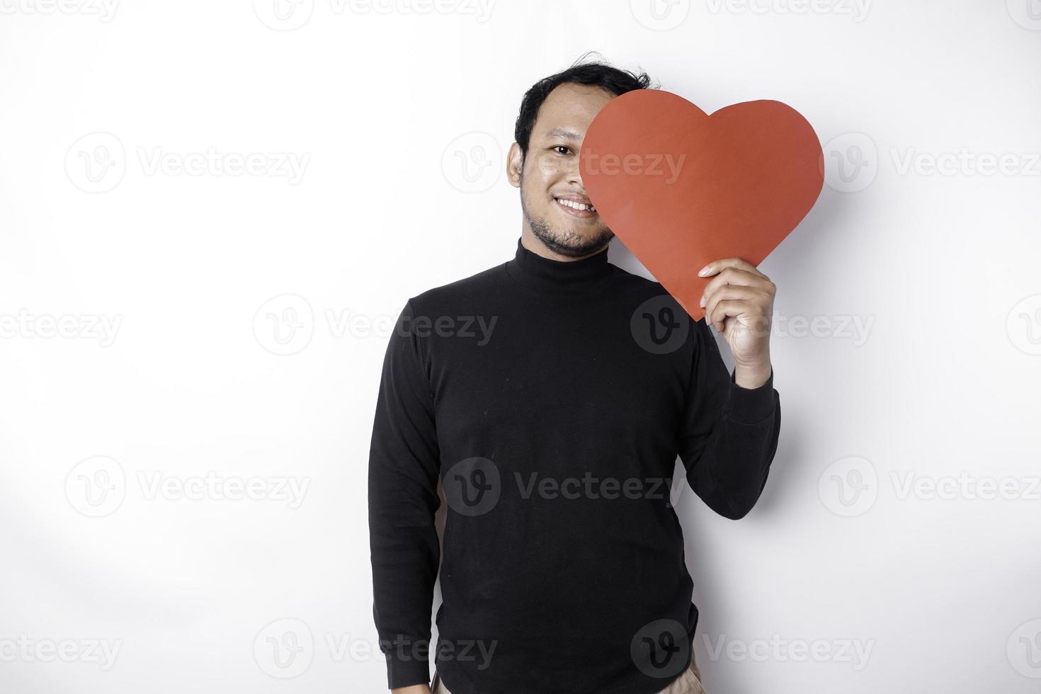 A portrait of a happy Asian man wearing a black shirt, holding a red heart-shaped paper isolated by white background photo