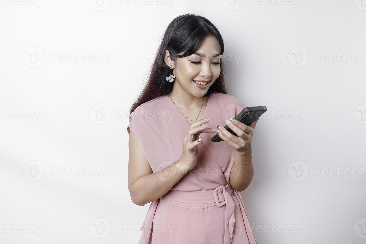 A portrait of a happy Asian woman dressed in pink and holding her phone, isolated by white background photo
