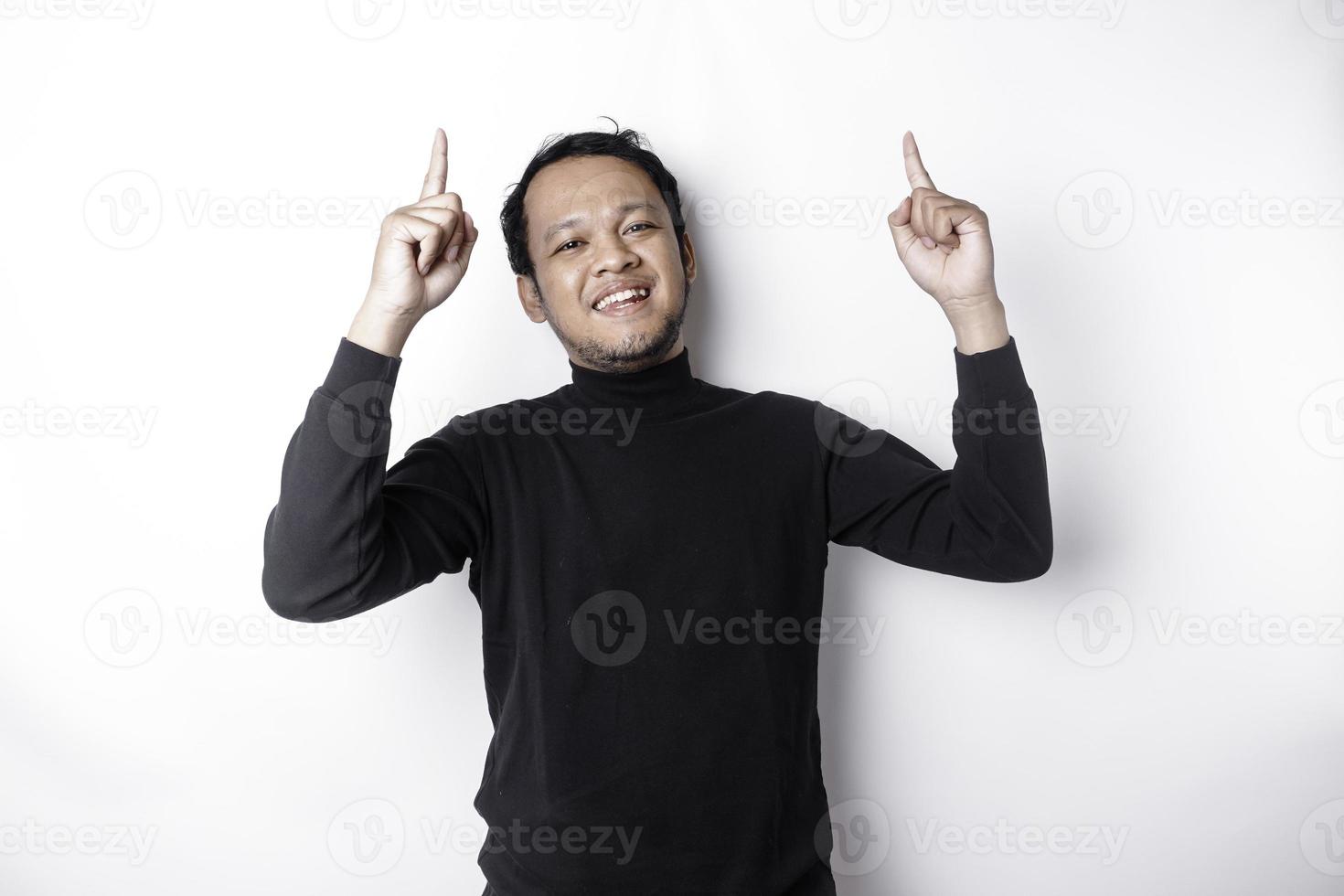 Excited Asian man wearing black shirt pointing at the copy space on top of him, isolated by white background photo