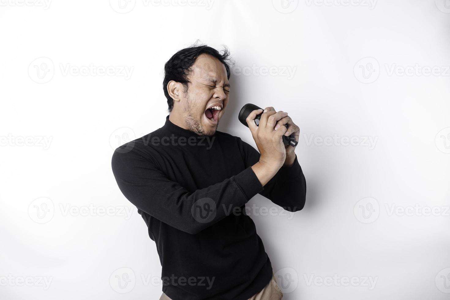 Portrait of carefree Asian man, having fun karaoke, singing in microphone while standing over white background photo