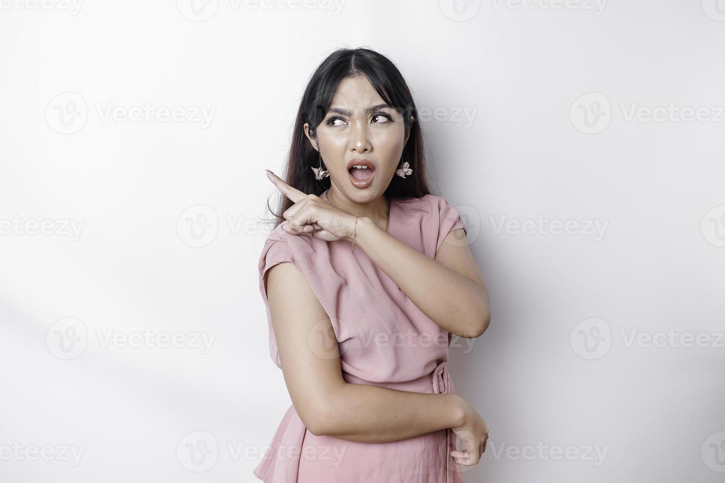 Questioned unaware young Asian pointing copy space beside her, look confused open mouth uncertain, being clueless, stand white background wear pink blouse photo