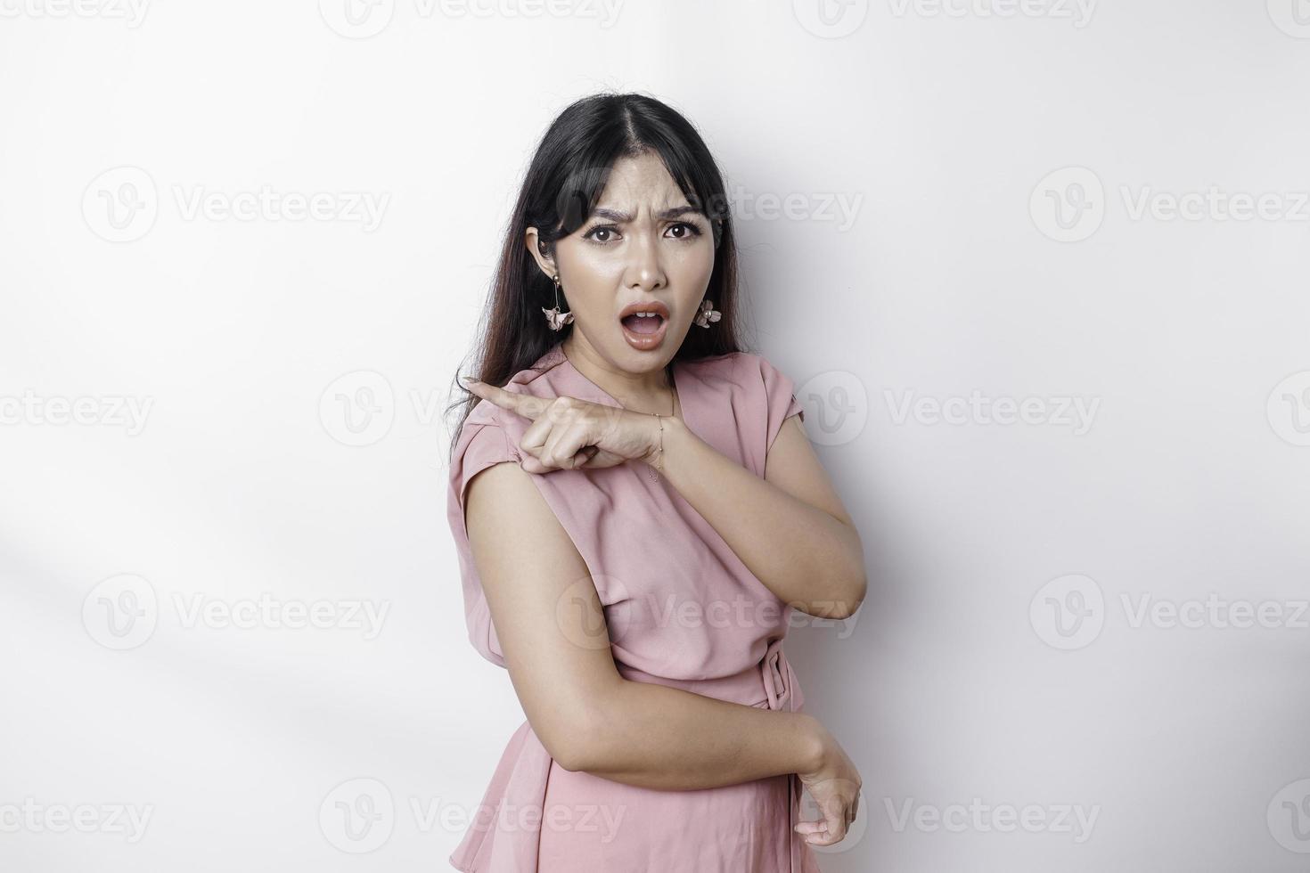 Questioned unaware young Asian pointing copy space beside her, look confused open mouth uncertain, being clueless, stand white background wear pink blouse photo