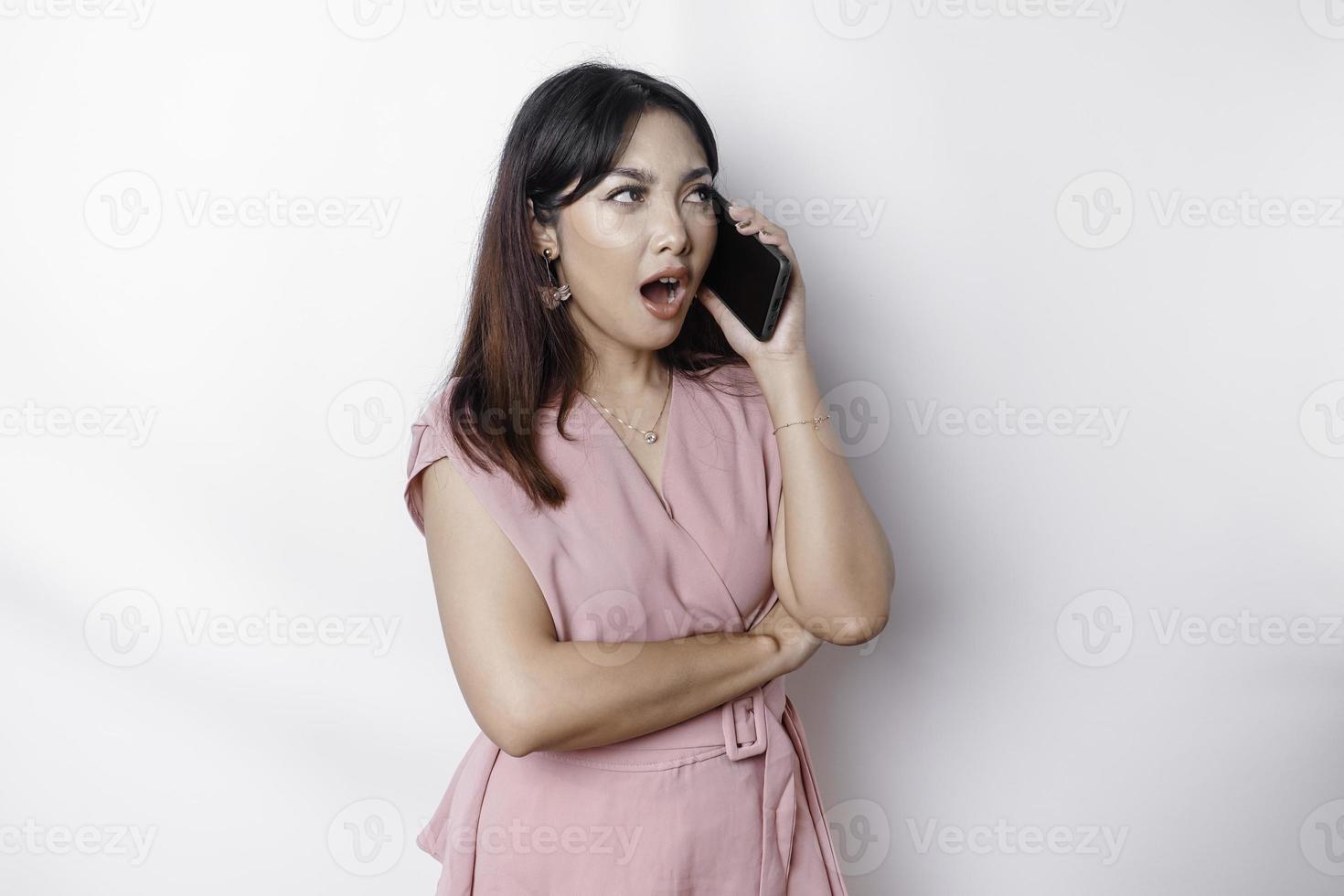 un insatisfecho joven asiático mujer vestido en rosa, mira descontento con irritado cara expresiones participación su teléfono foto