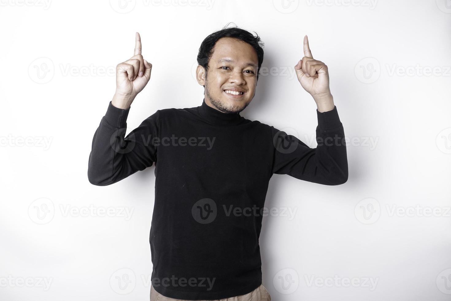 Excited Asian man wearing black shirt pointing at the copy space on top of him, isolated by white background photo