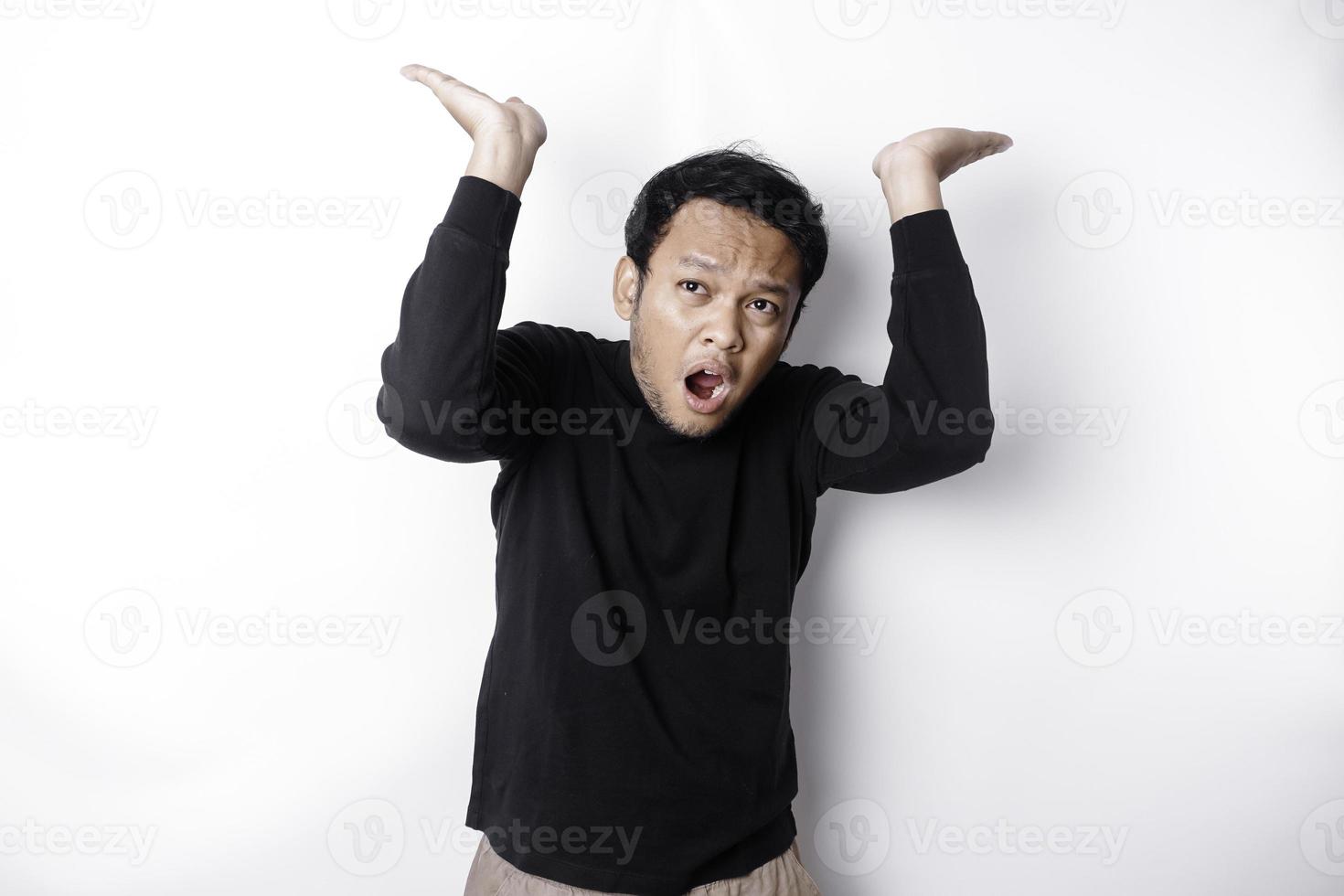 conmocionado asiático hombre vistiendo negro camisa señalando a el Copiar espacio en parte superior de a él, aislado por blanco antecedentes foto