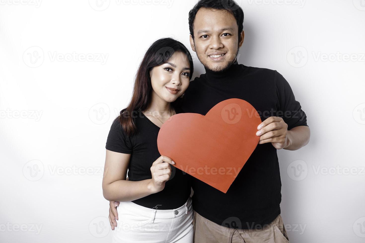 un joven asiático Pareja sonriente y participación rojo en forma de corazon papel, aislado por blanco antecedentes foto