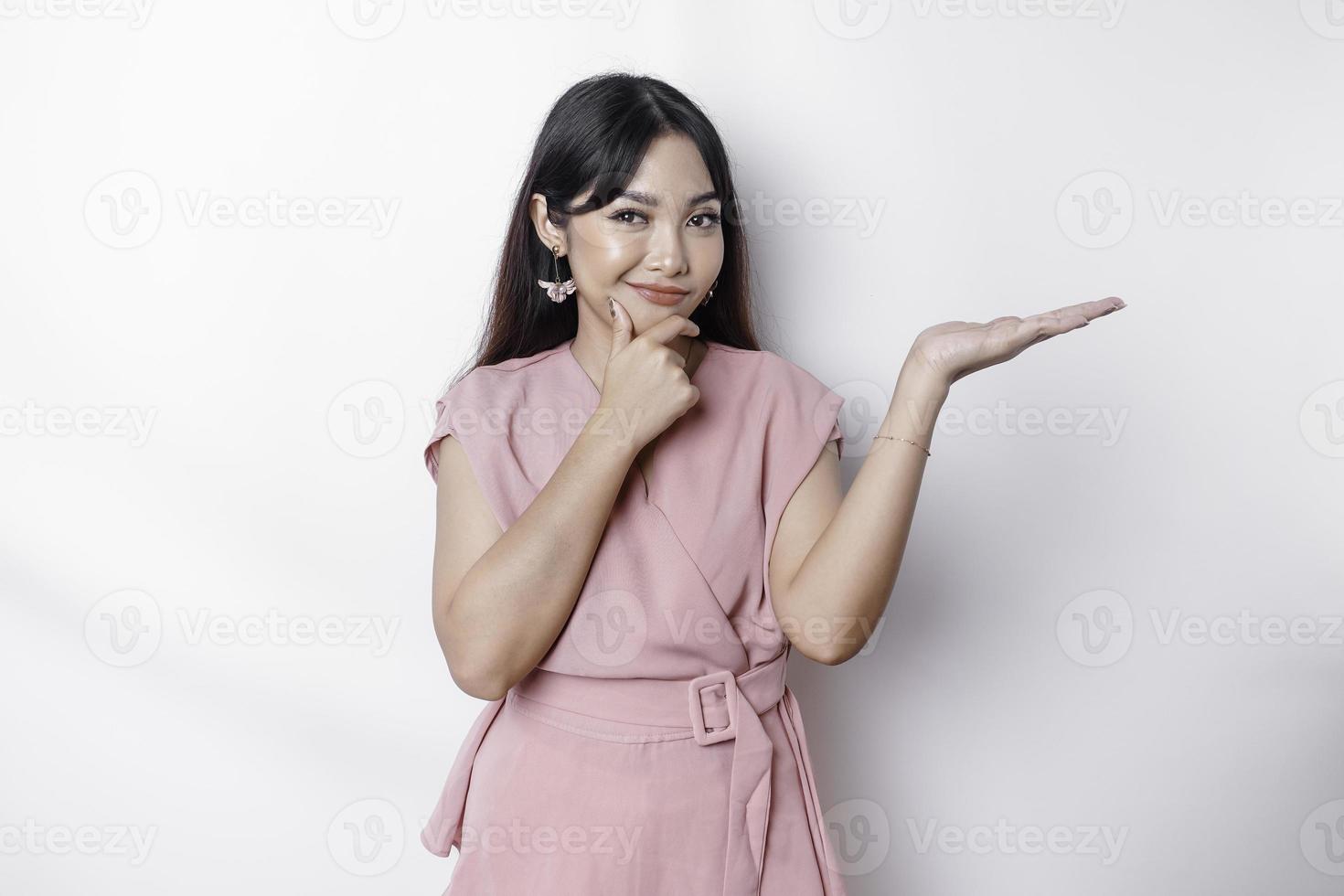 A thoughtful young woman dressed in pink and holding her chin while pointing copy space beside her, isolated by white background photo