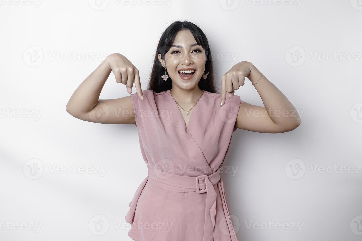 emocionado asiático mujer vestido en rosa, señalando abajo a el Copiar espacio, aislado por blanco antecedentes foto