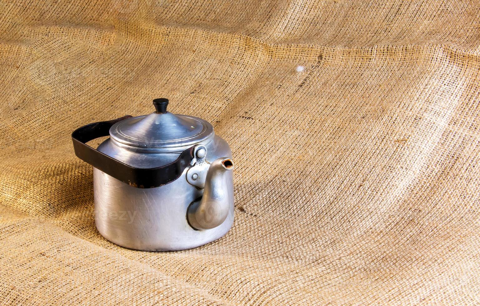 An old soldier's aluminum teapot from the Second World War against the background of burlap. photo