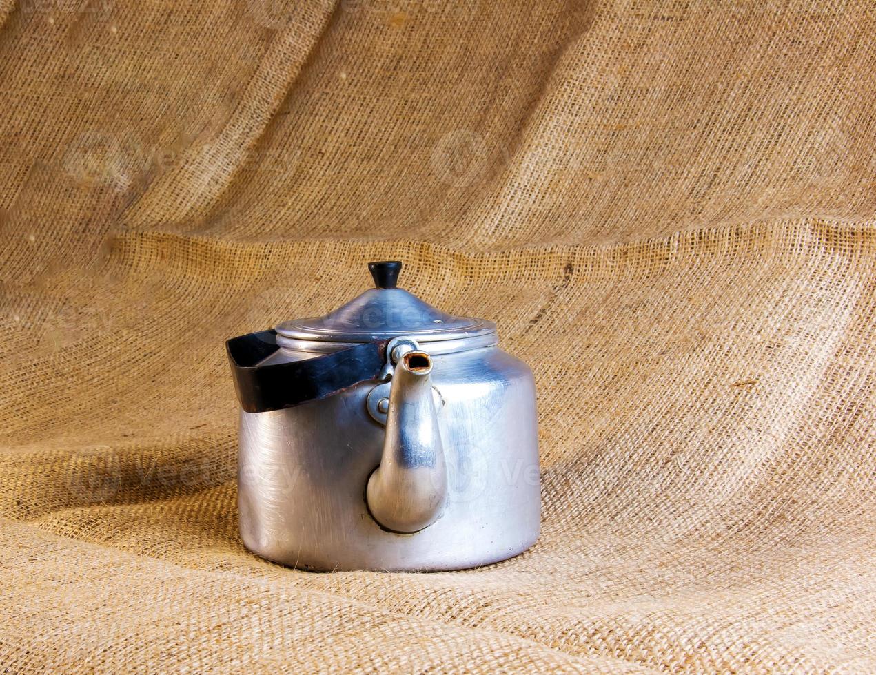 An old soldier's aluminum teapot from the Second World War against the background of burlap. photo