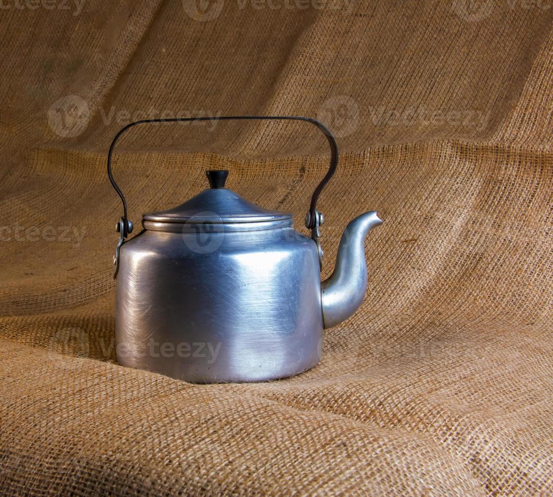 An old soldier's aluminum teapot from the Second World War against the background of burlap. photo