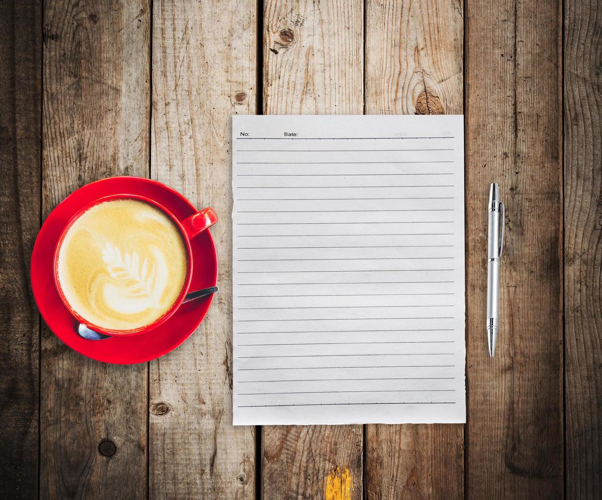Empty paper and pen with red cup coffee on wood table background photo