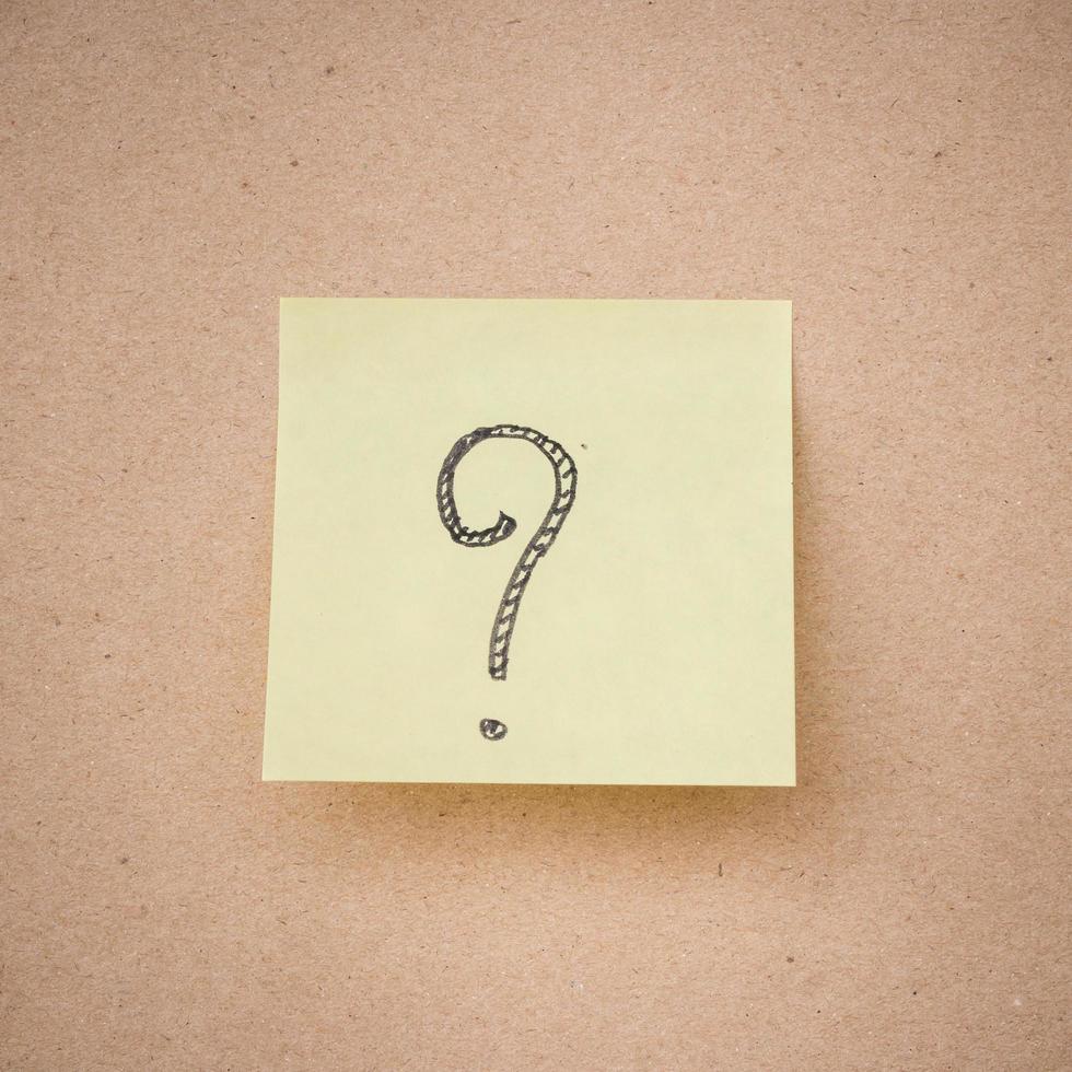 yellow sticky note question mark on brown paper texture close up photo