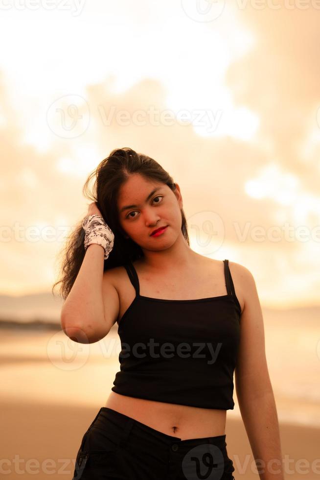 un asiático adolescente en un negro camisa es visto en pie en el playa mientras en vacaciones a el playa foto