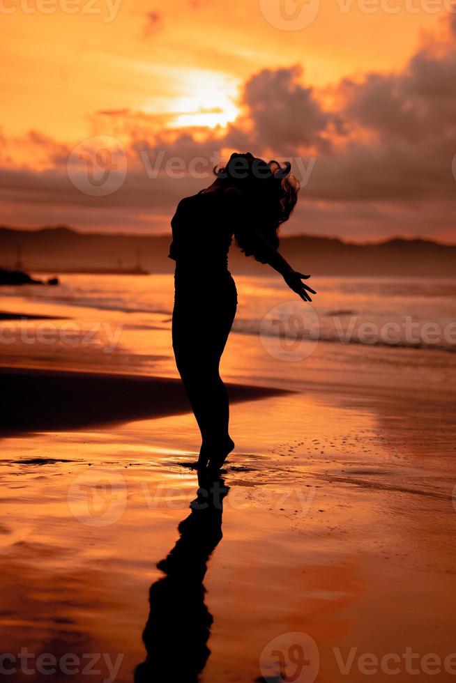 an Asian woman in silhouette is doing a very beautiful dance on the beach with the waves crashing photo