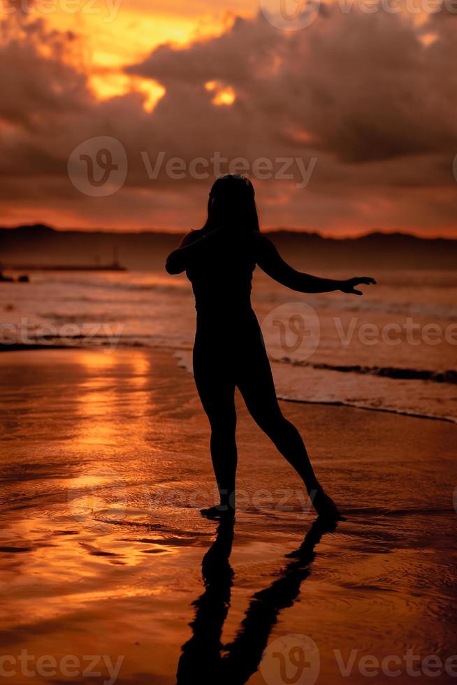 silhouette of an Asian woman dancing ballet with great flexibility and a view of the waves behind her photo