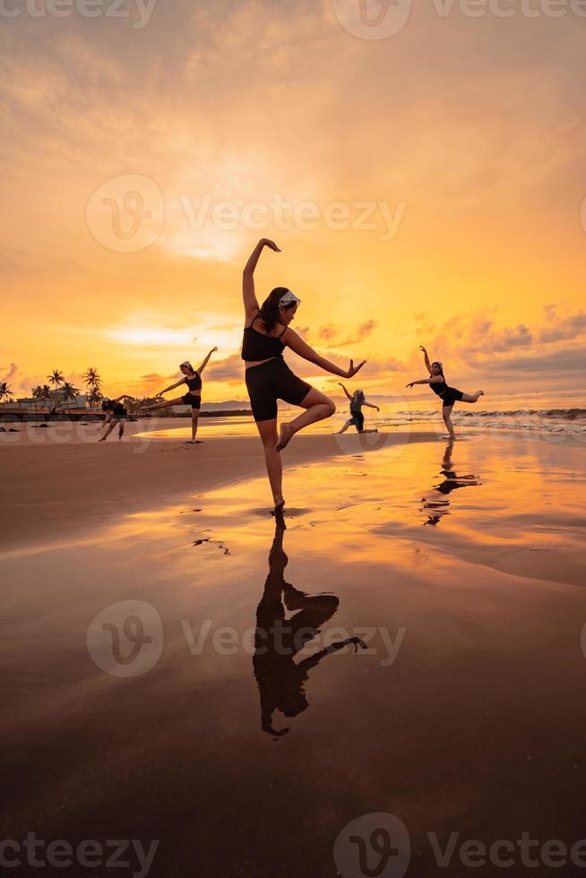 a group of Asian women is standing on the beach in black clothes and doing ballet moves in unison photo