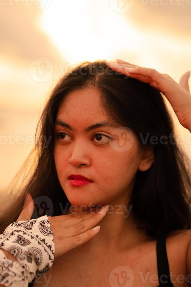 An Asian woman with long black hair poses with her hands while enjoying the view of the beach photo