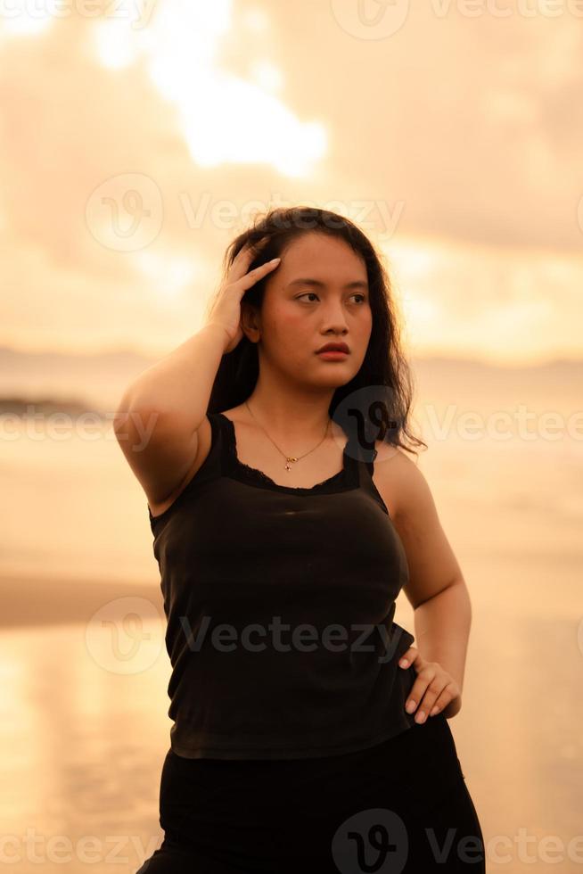 portrait image of an Asian woman with black hair and an angry expression standing on the beach in her black clothes photo