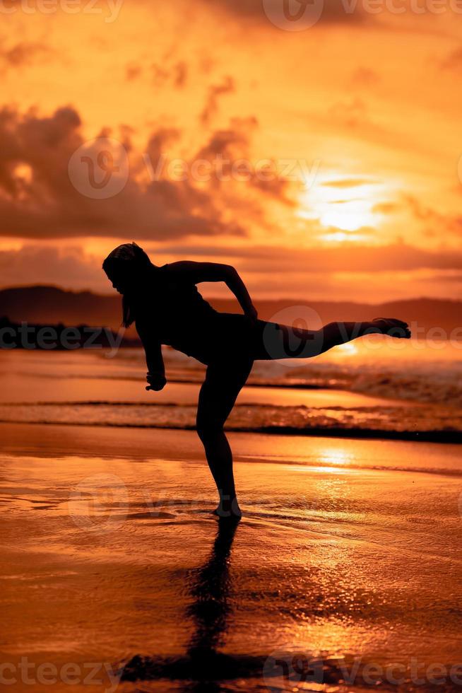 silhouette of an Asian woman dancing ballet with great flexibility and a view of the waves behind her photo