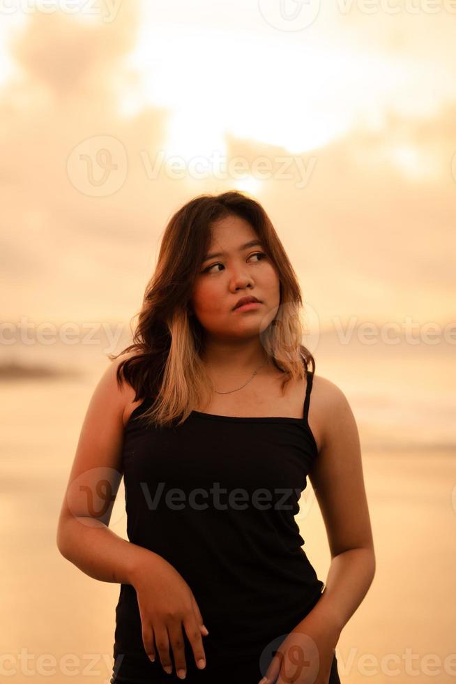 An Asian woman poses with a dirty and angry expression when wearing a black dress on the beach photo