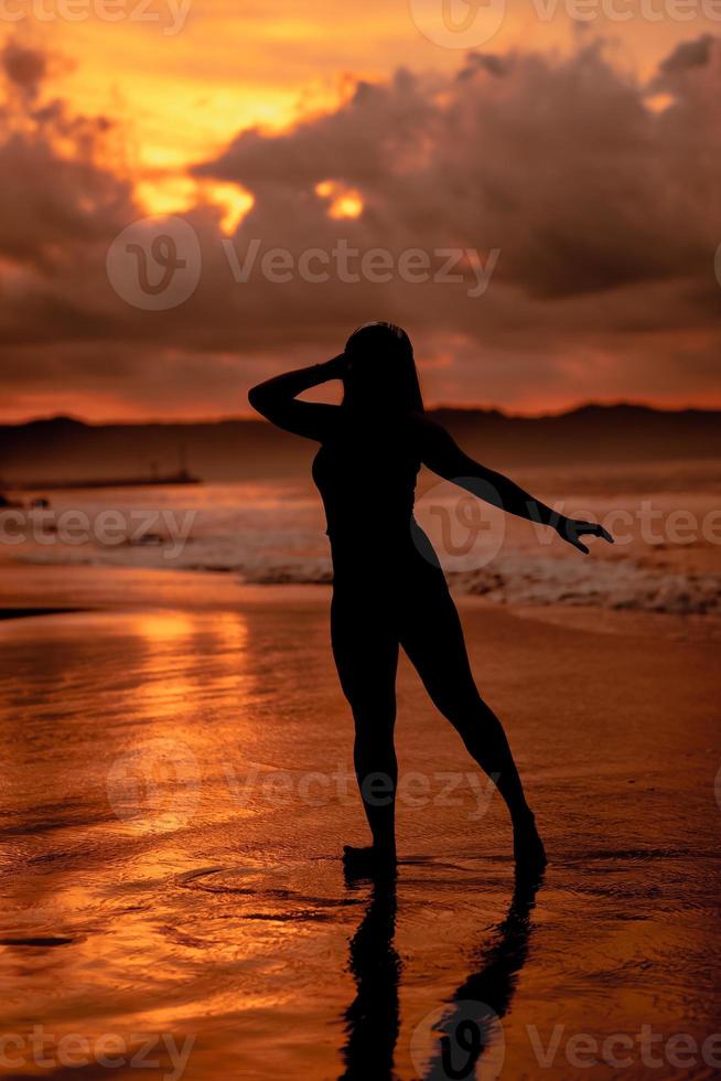 silhouette of an Asian woman dancing ballet with great flexibility and a view of the waves behind her photo