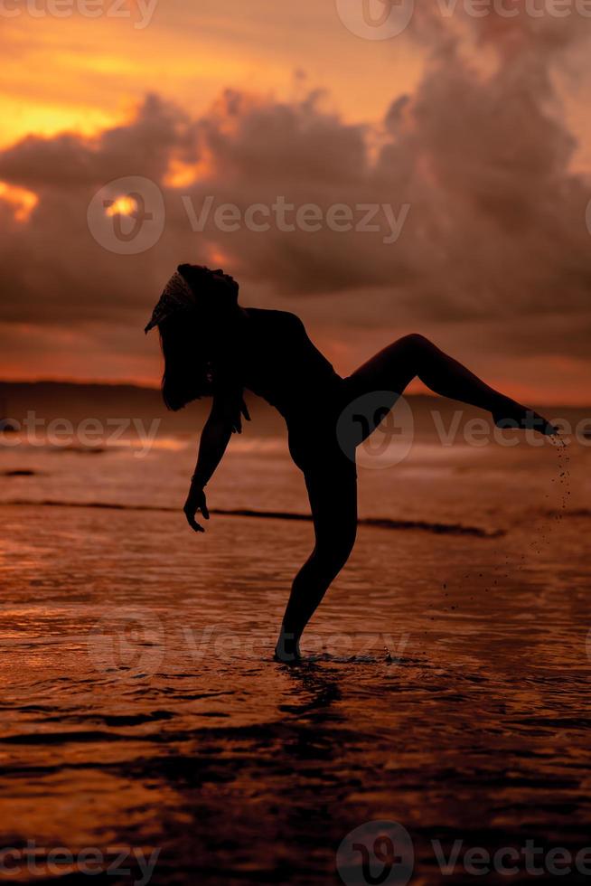 silueta de un asiático mujer jugando en el agua en el playa con fuerte olas estrellarse foto