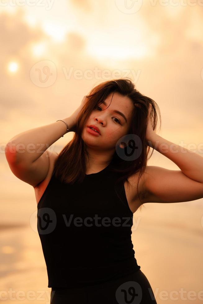 an Asian teenager who is posing sexy by holding her head and black hair on the beach photo