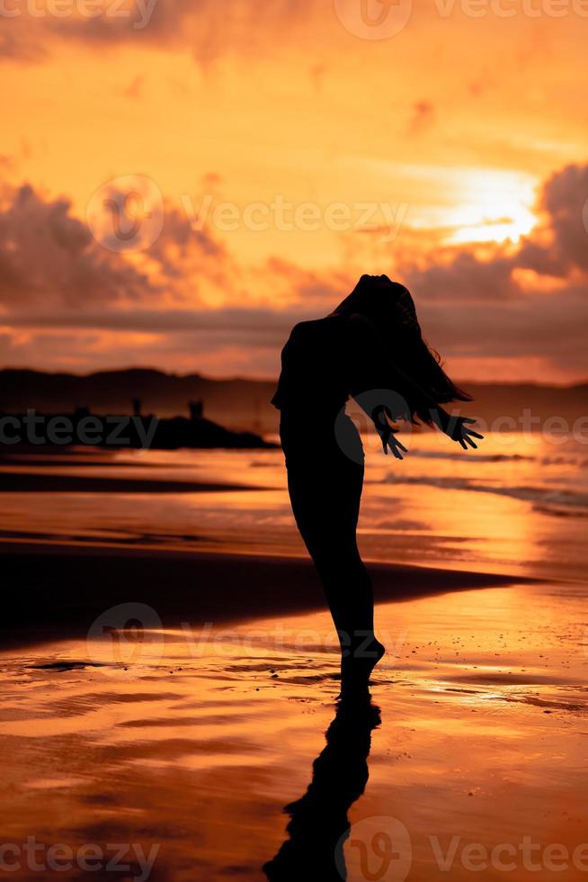 an Asian woman in silhouette is doing a very beautiful dance on the beach with the waves crashing photo