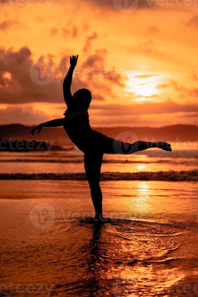 silhouette of an Asian woman dancing ballet with great flexibility and a view of the waves behind her photo