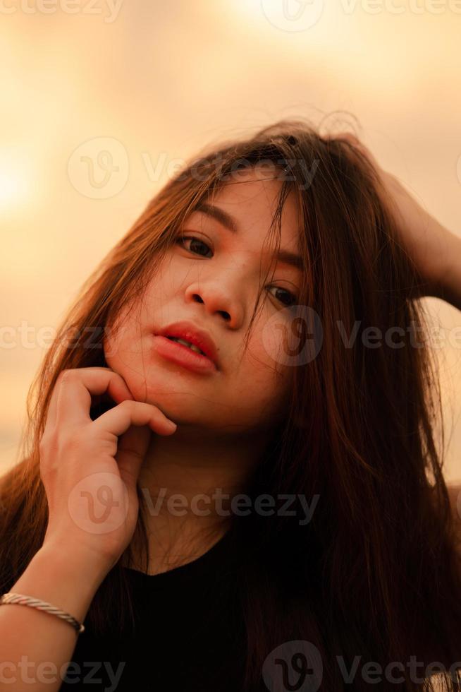 un hermosa y sexy asiático mujer con un facial expresión ese mira desordenado arriba mientras en pie en el playa foto