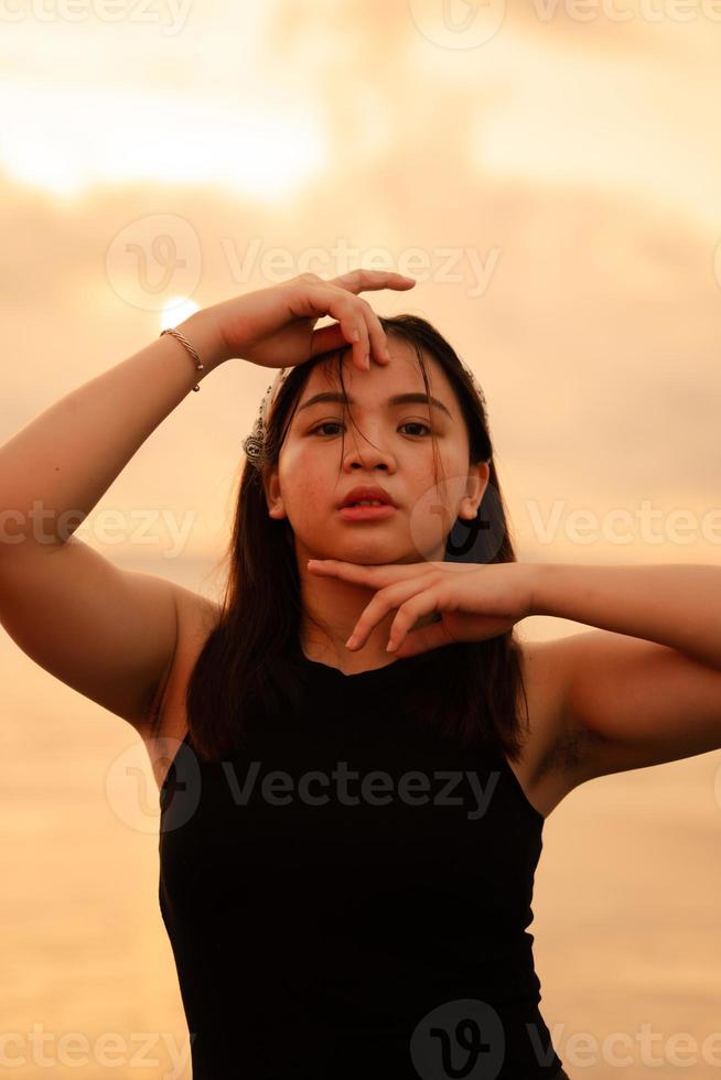 a glamorous Asian woman in black clothes and a white bandana standing in front of the waves on the beach photo