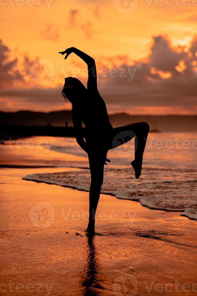 An Asian woman in the form of a silhouette doing ballet movements very agile on the beach photo