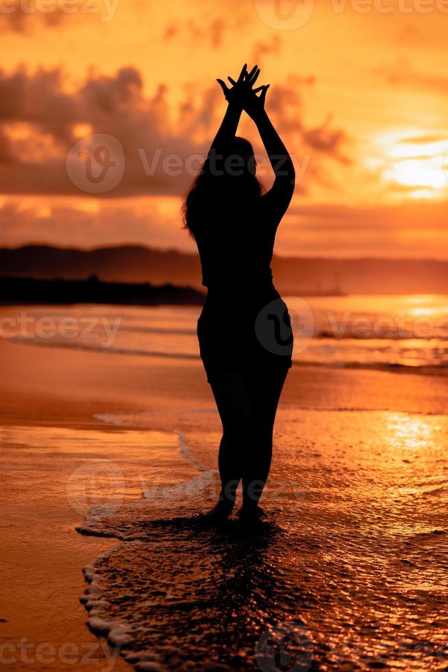 the silhouette of an Asian teenager with a tall body is dancing ballet on the waves on the beach photo