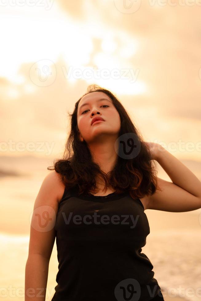 un asiático mujer posando muy sexy mientras vistiendo negro ropa en el playa foto